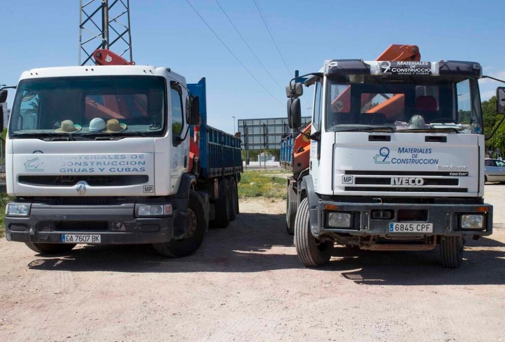 Dos camiones grúa de Calería Los 9 rotulados con «Materiales de construcción, grúas y cubas»
